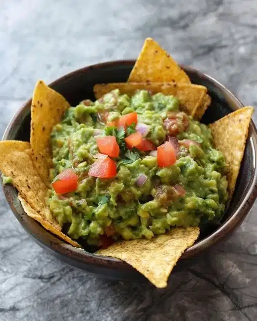 Bol de guacamole frais avec des chips de tortilla et des ingrédients frais